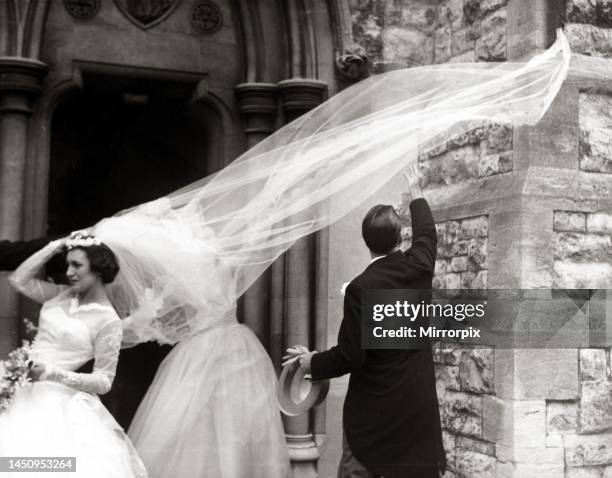 Racing driver Jack Brabham tries to catch the bride's windswept veil at the wedding ceremony of his manager Phil Kerr and Valerie Triggs, at St...