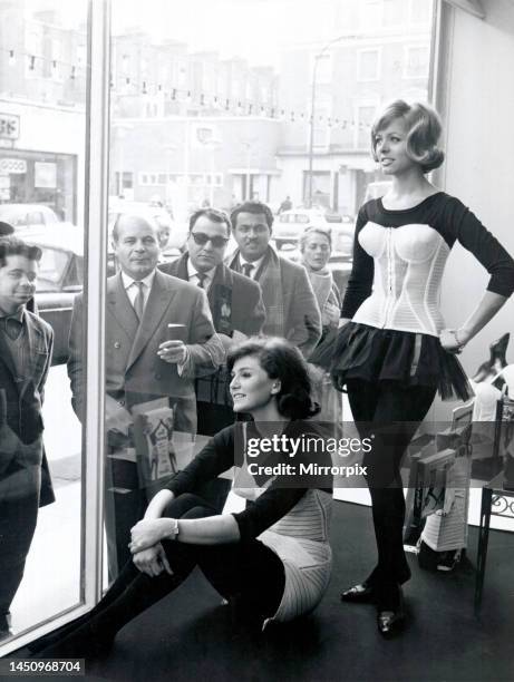 Two women modelling corsets in shop window while people on the street look in. 8th March 1963.