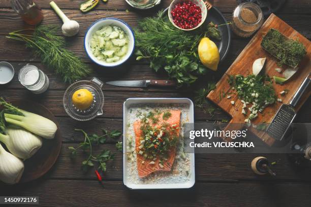 cooking preparation of salmon fish fillet on dark rustic kitchen table with utensils and  various healthy ingredients: lemon, herbs and spices - recipe stock pictures, royalty-free photos & images