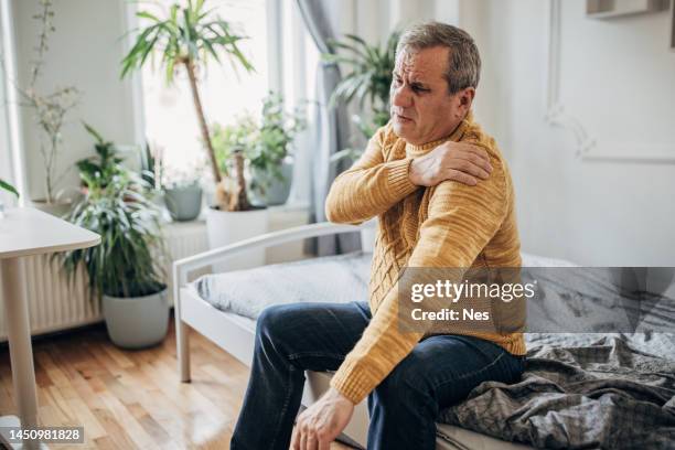 a man holds a hand on a sick shoulder - only senior men stock pictures, royalty-free photos & images
