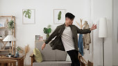 asian male young adult having fun dancing in style at a modern white living room in his apartment.