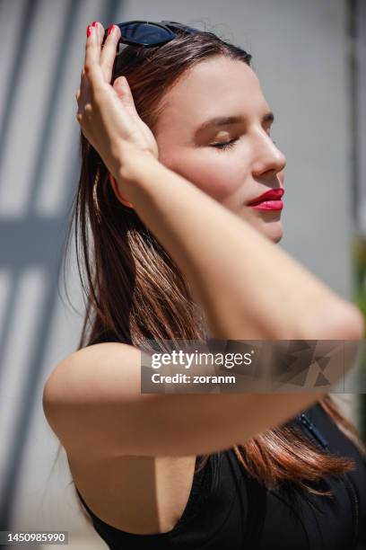 portrait of beautiful young woman in black sleeveless top enjoying sunlight with eyes closed - sleeveless dress stock pictures, royalty-free photos & images