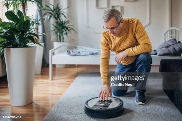 a senior uses a robotic vacuum cleaner - vacuum cleaner stock pictures, royalty-free photos & images