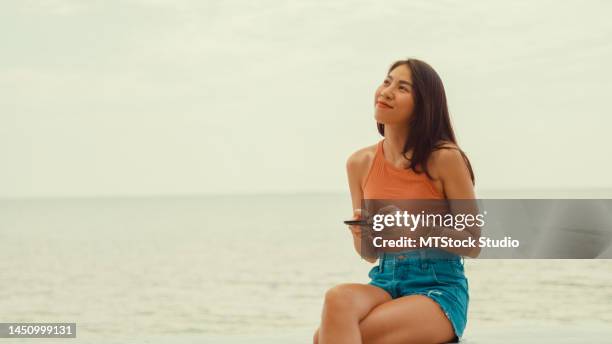 young asian woman using smartphone on tropical beach. - hammamet beach stock pictures, royalty-free photos & images