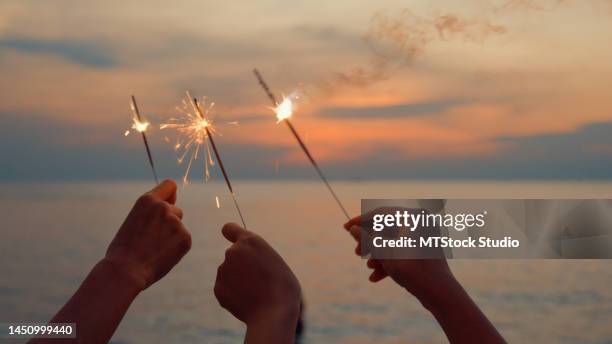 close up hand of young asian women celebrating holding sparklers on tropical beach at sunset. - onafhankelijkheidsdag stockfoto's en -beelden