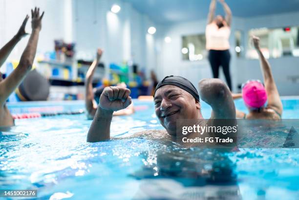 portrait of a senior man with left arm amputation during a group fitness class at swimming pool - adult swim imagens e fotografias de stock