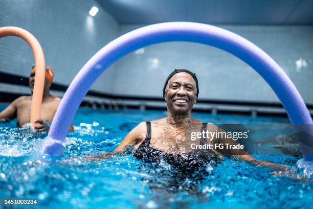 portrait of a senior woman exercising with noodle float at swimming pool - aquarobics stock pictures, royalty-free photos & images
