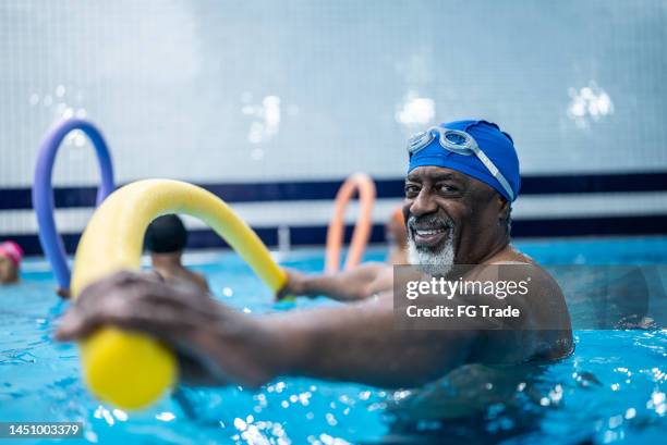 portrait of a senior man doing exercise with noodle float at swimming pool - aqua aerobics stock pictures, royalty-free photos & images