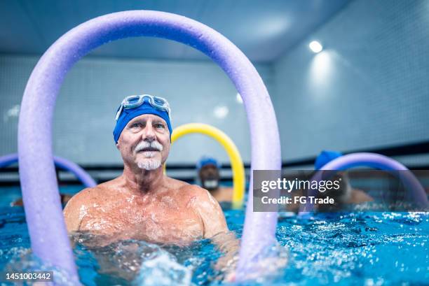 älterer mann trainiert mit nudelschwimmer im schwimmbad - aquarobics stock-fotos und bilder