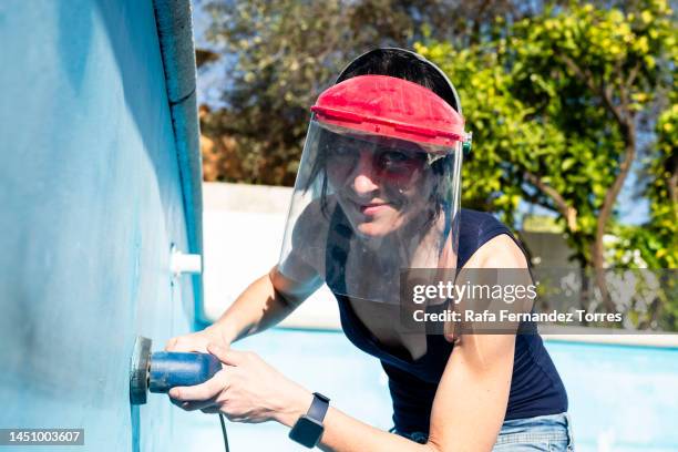 woman wearing protective mask using sander on swimming pool wall - swimming pool maintenance stock pictures, royalty-free photos & images