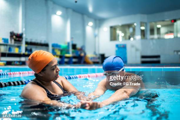 senior man learning to swim in a swimming pool - aqua aerobics stockfoto's en -beelden