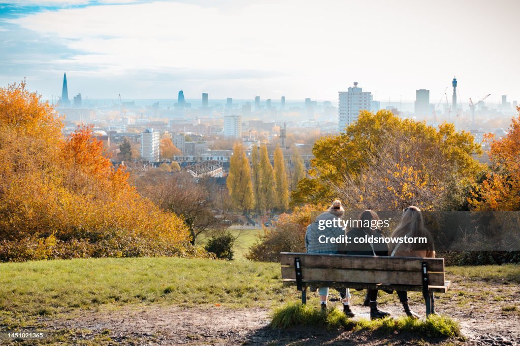 Women sitting on park bench looking at London city skyline from Hampstead Heath