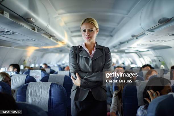 smiling female flight attendant among seats in a plane. - airhostess stock pictures, royalty-free photos & images