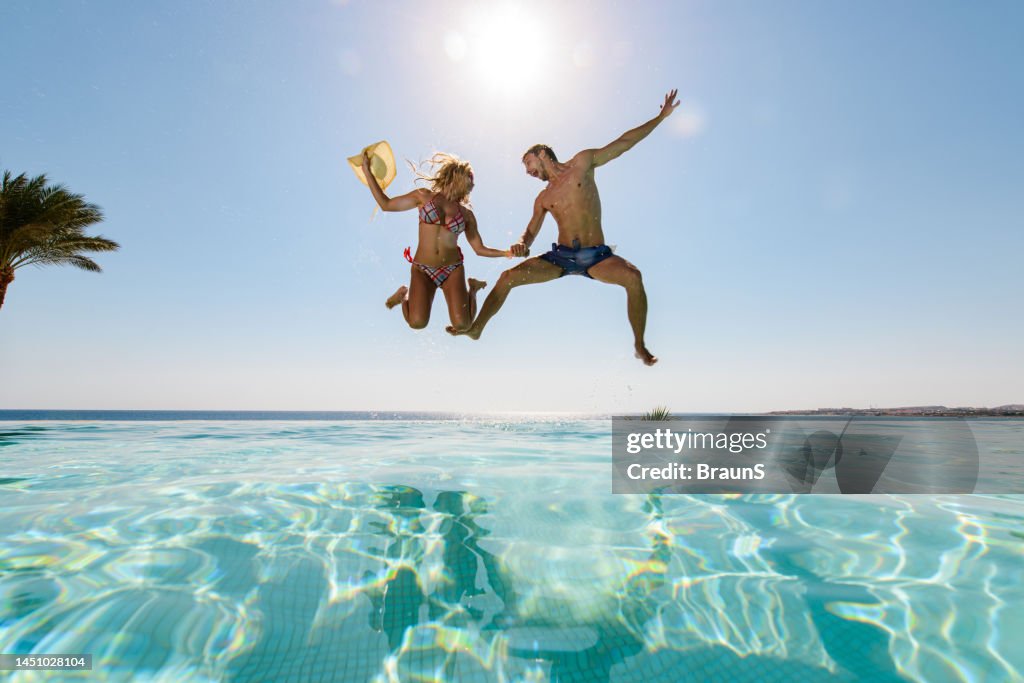 Below view of playful couple jumping into infinity pool.