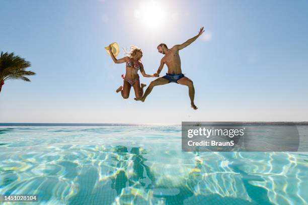 below view of playful couple jumping into infinity pool. - jumping sun stock pictures, royalty-free photos & images