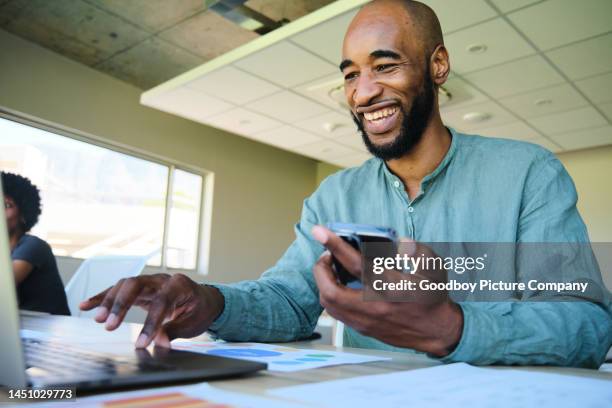 laughing businessman checking his phone while working on a laptop - file sharing stock pictures, royalty-free photos & images