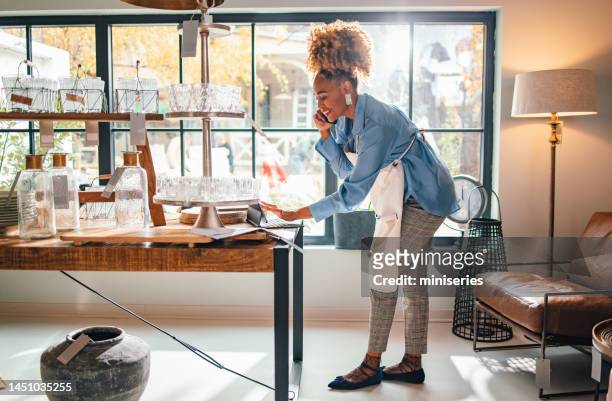 smiling business woman talking on a mobile phone in her store - small business stock pictures, royalty-free photos & images