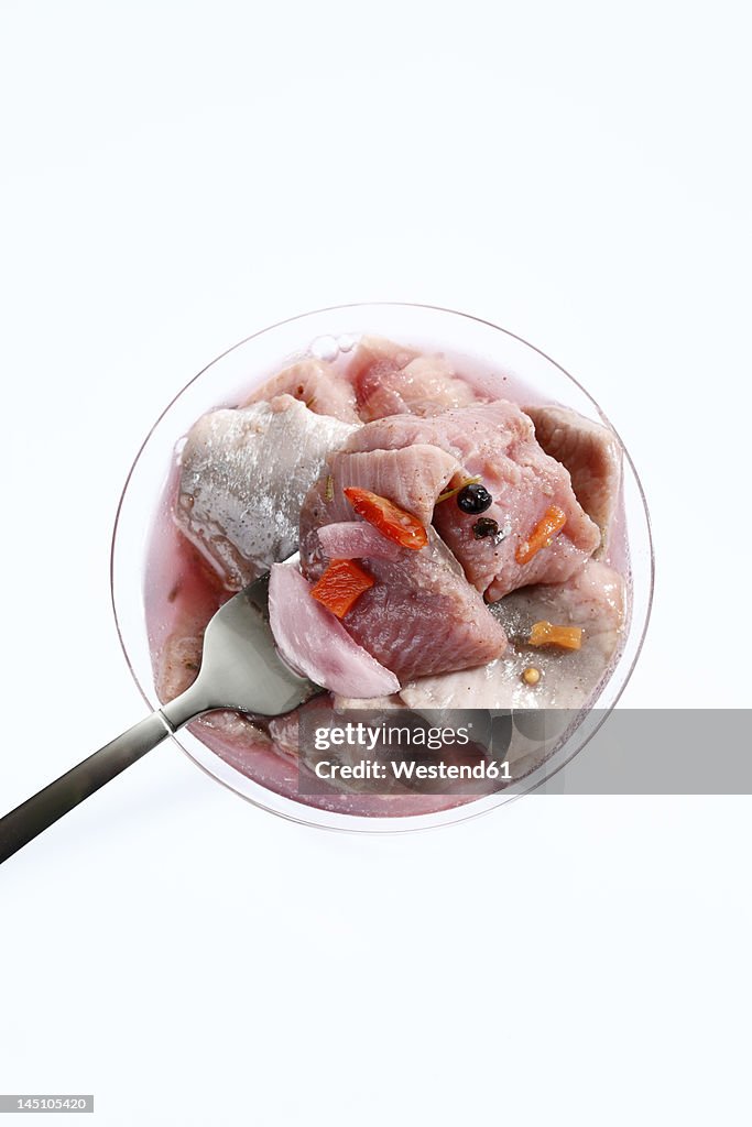 Salted herring in glass with fork against white background, close up