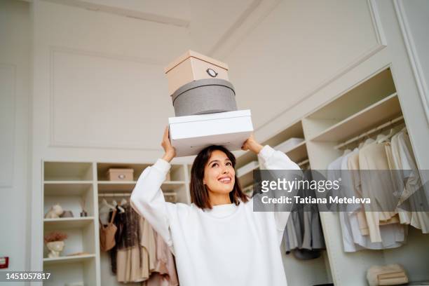 housekeeping and moving clothes boxes. smiling woman carrying clothes boxes on her head near walk in wardrobe - entrümpeln stock-fotos und bilder