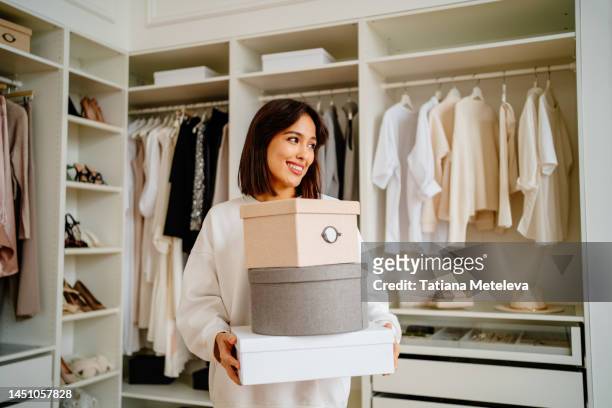 get rid of excess clothes. smiling woman carrying clothes boxes in hands near walk in wardrobe - huishoudelijk werk stockfoto's en -beelden