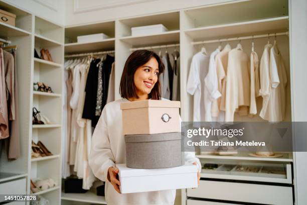 get rid of excess clothes. smiling woman carrying clothes boxes in hands near walk in wardrobe - designer shopping stock pictures, royalty-free photos & images