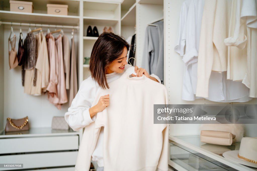 Smiling woman holding and cleaning woolen sweater on hanging in the closet
