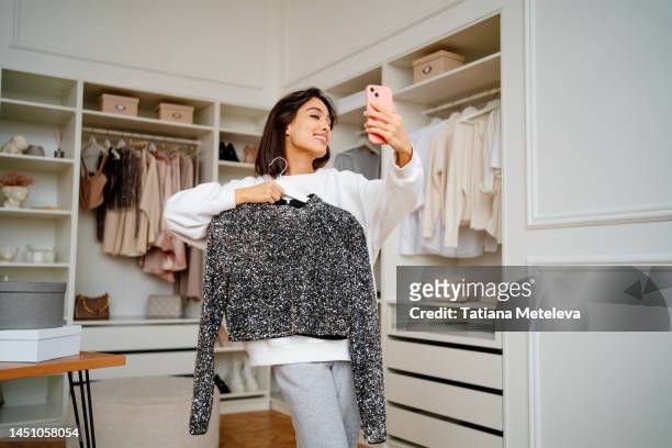 female vlogger advertising and presenting new fashionable shirt on rack by smartphone - sponsor stockfoto's en -beelden