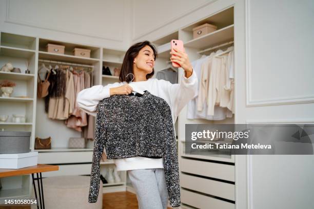 female vlogger advertising and presenting new fashionable shirt on rack by smartphone - showing off - fotografias e filmes do acervo