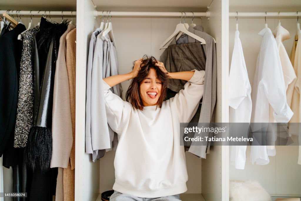 What a mess, clothes outfit problem. Laughing hysterical female standing in the wardrobe in trouble