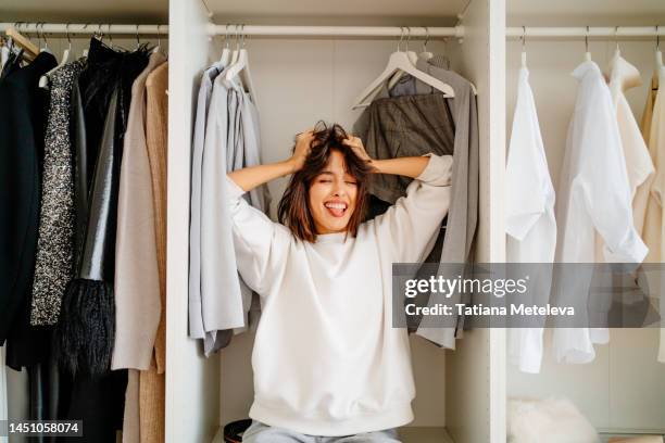 what a mess, clothes outfit problem. laughing hysterical female standing in the wardrobe in trouble - clothes wardrobe stockfoto's en -beelden