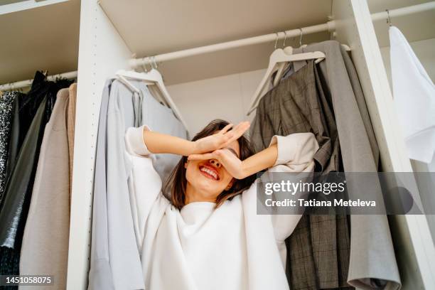difficult decision of clothes. funny dramatic female arms covering her face, standing in the closet - kleiderschrank stock-fotos und bilder