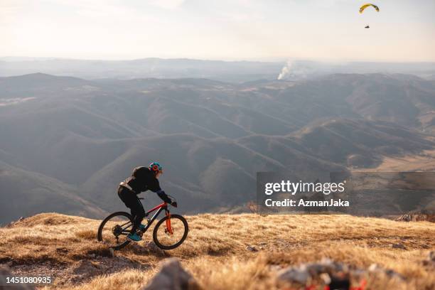 adulto ciclista di montagna maschio caucasico che cavalca una bicicletta in cima alla collina circondata da una splendida natura e una vista incredibile - paracadutista foto e immagini stock