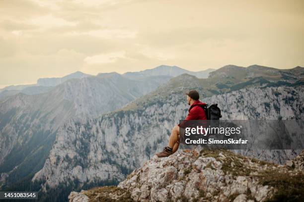 männlicher wanderer, der die malerische aussicht genießt, während er auf dem gipfel des berges sitzt - confidence male landscape stock-fotos und bilder