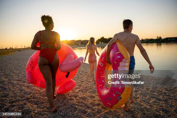 friends with inflatable rings walking towards lakeshore - slovenia beach stock pictures, royalty-free photos & images
