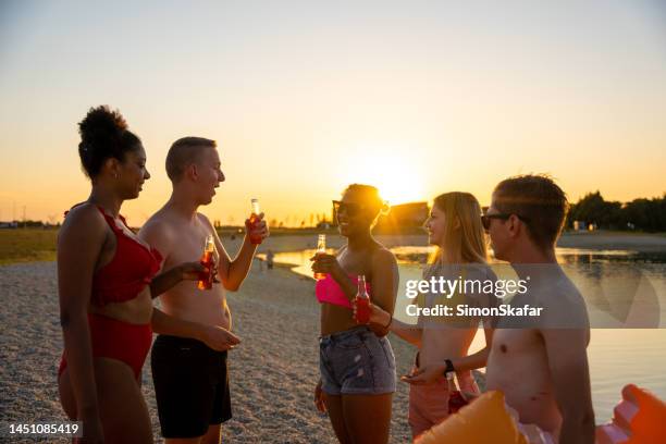 friends talking and enjoying beer at lakeshore during sunset - slovenia beach stock pictures, royalty-free photos & images