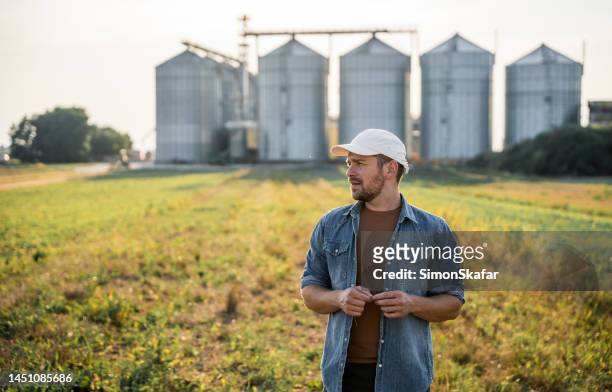 male farmer standing in front of silos in field - agrarisch gebouw stockfoto's en -beelden