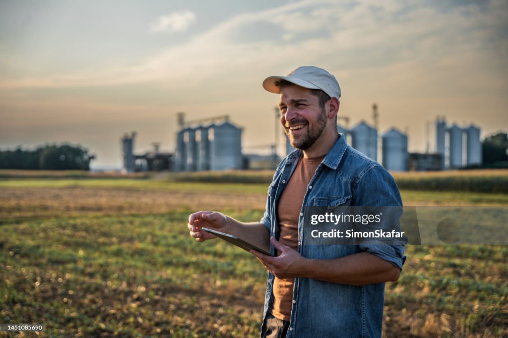 Feliz agricultor masculino usando tableta digital en el campo contra el cielo