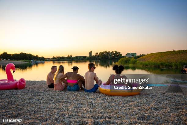 friends talking and relaxing at lakeshore during sunset - slovenia beach stock pictures, royalty-free photos & images