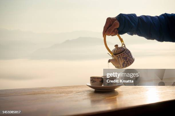 senior's hand pouring chinese tea into white cup background with foggy sunrise in the mountains. - traditional ceremony stock-fotos und bilder