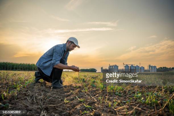 male farmer checking soil at agricultural field against sky - metallic jacket stock pictures, royalty-free photos & images