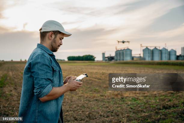 male farmer with remote controller flying drone above farmland - farmer drone stock pictures, royalty-free photos & images