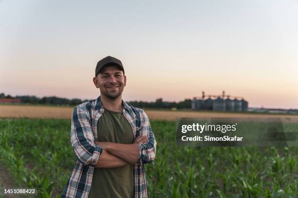 happy male farmer standing with arms crossed in corn field - agriculture happy stockfoto's en -beelden