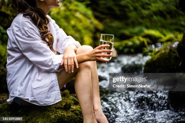 mittelteil der frau, die trinkwasser am fließenden fluss hält - drinking water glass woman stock-fotos und bilder