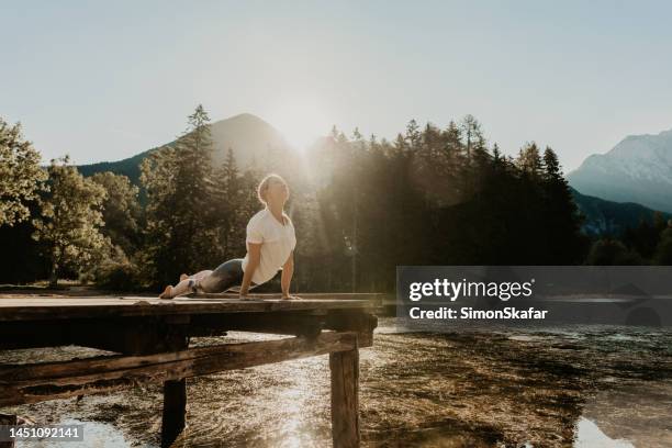 woman practicing cobra pose on pier over lake in forest during sunset - forest cobra stock pictures, royalty-free photos & images