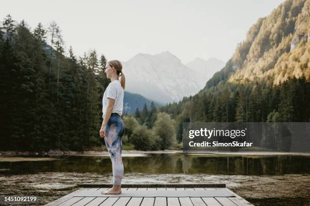 side view of woman in mountain pose standing on pier by lake - boa postura imagens e fotografias de stock