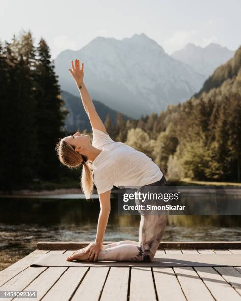 weiblicher yogi mit handerhobener kamelpose auf dem pier bei sonnenuntergang - woman stretching sunset stock-fotos und bilder