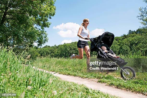 germany, munich, mother jogging with baby boy in pram, smiling - jogging stroller stockfoto's en -beelden