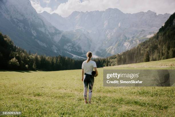 vista trasera de una mujer con colchoneta de ejercicios mirando a las montañas - yogi fotografías e imágenes de stock