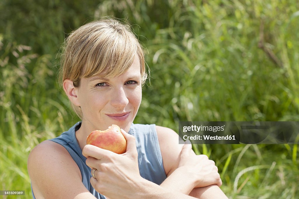 Germany, Bavaria, Mid adult woman eating apple, smiling, portrait