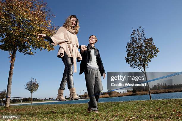 germany, bavaria, munich, woman on slackline with man, smiling - woman tightrope stock pictures, royalty-free photos & images